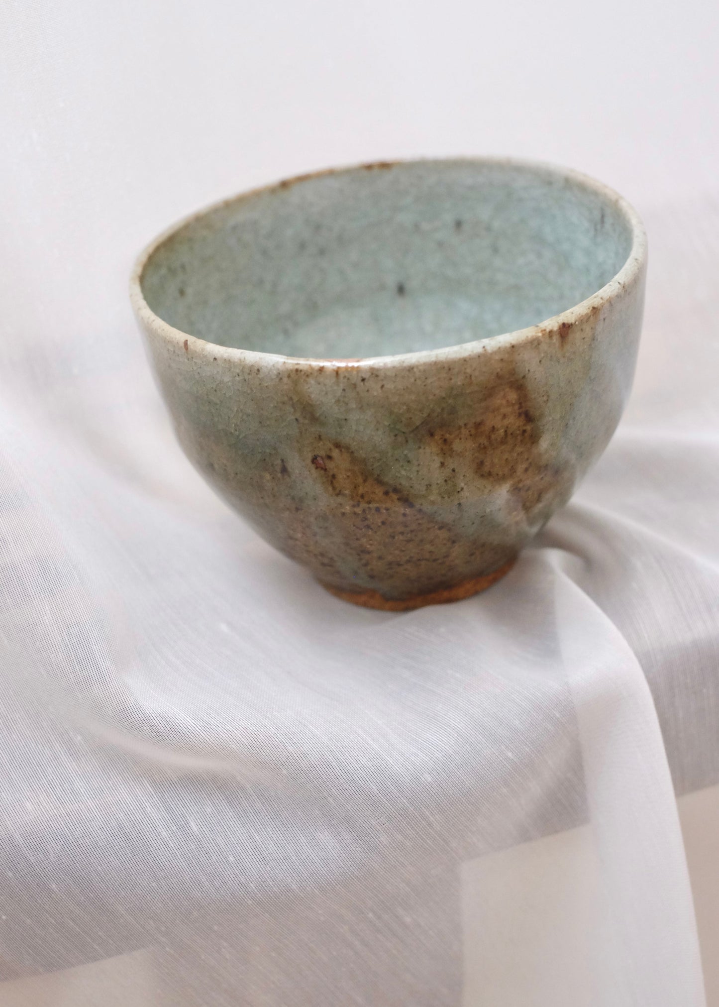 Ceramic celadon bowl with a textured surface on a sheer white fabric background