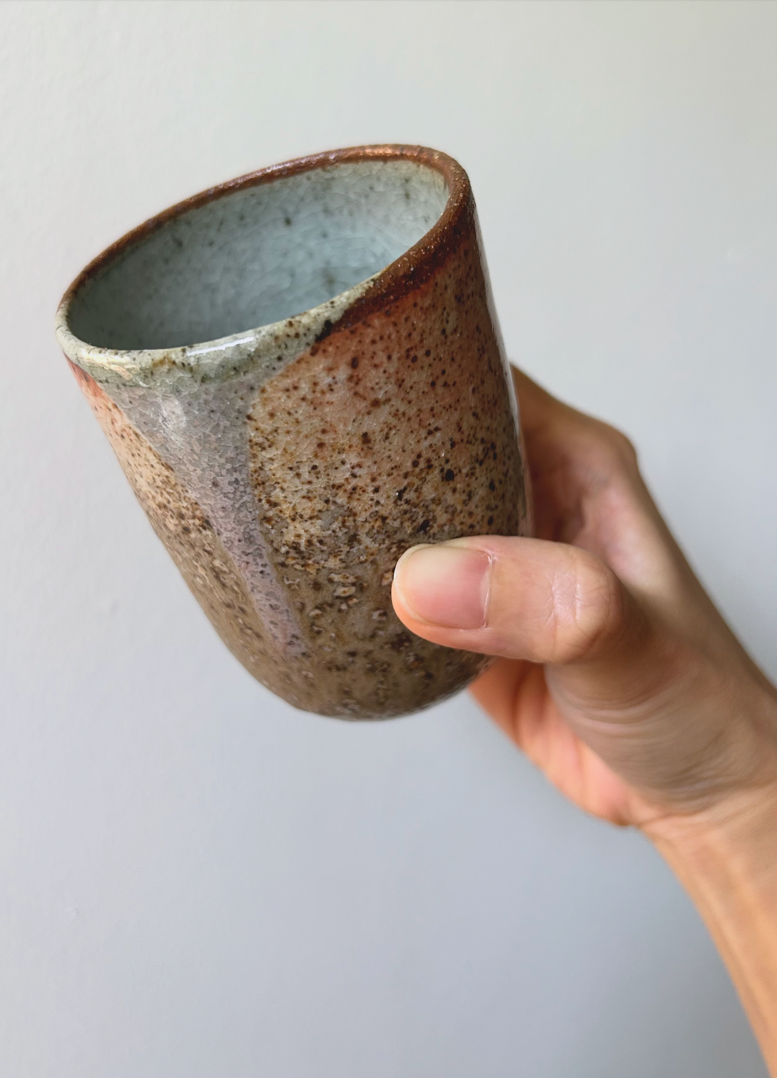 Hand holding a ceramic cup with a speckled texture against a plain background