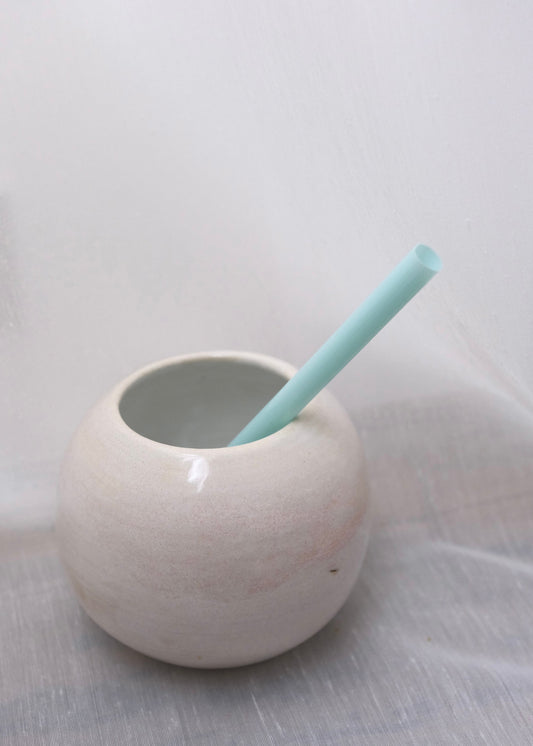 White ceramic coconut-shaped cup with a light blue straw on a white background