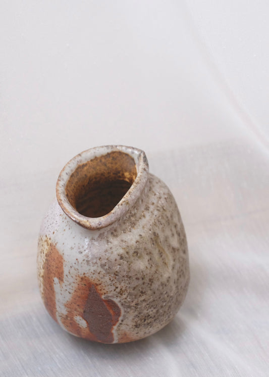 Assymetrical ceramic bud vase with brown and beige speckled glaze on a sheer white background